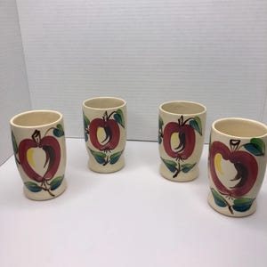 May include: Set of four vintage ceramic mugs with a hand-painted apple design. The mugs are white with red, yellow, and green accents.