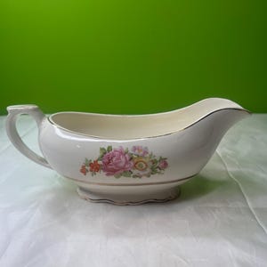 Puede incluir: Salsera de color crema con un diseño floral con rosas rosas y amarillas. La salsera tiene un asa y un pico, con ribete dorado. Una pieza clásica para servir salsas y salsas.