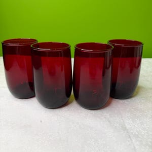 Puede incluir: Cuatro vasos de beber sin pie de color rojo oscuro, con un tono más oscuro en la base. Los vasos tienen forma cilíndrica con la base redondeada. El fondo es de color verde liso.