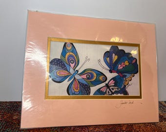May include: A framed art print featuring three colorful butterflies with intricate patterns and details. The butterflies are painted in shades of blue, green, pink, and yellow. The print is signed "Jaide" in the bottom right corner.