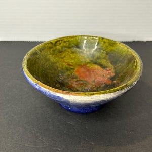 May include: A small, green, blue and white ceramic bowl with a glazed finish. The bowl has a rounded shape and a slightly flared rim.