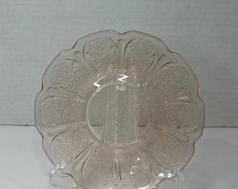 May include: A pink glass saucer with a scalloped edge and a floral pattern.