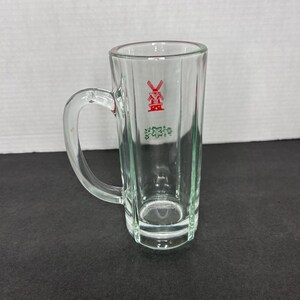 May include: A clear glass mug with a handle. The mug has a red windmill logo with the text "De Molen" in green.