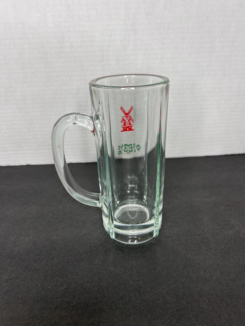 May include: A clear glass mug with a handle. The mug has a red windmill logo with the text "De Molen" in green.