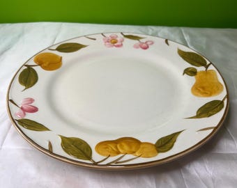 May include: White ceramic plate with a gold rim, decorated with yellow fruit, green leaves, and pink flowers. The plate has a simple, elegant design, suitable for serving food.