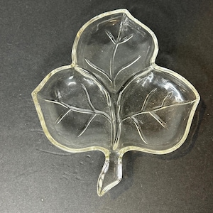 Puede incluir: Un plato de vidrio transparente en forma de hoja con tres secciones. El plato está diseñado para parecer un trébol de tres hojas.