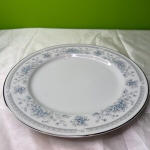 Puede incluir: Plato de porcelana blanco con borde plateado y un estampado floral en tonos azules. El plato presenta un delicado diseño de flores y hojas azules alrededor del borde, adecuado para servir comidas.