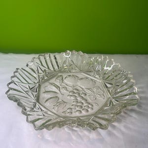 Op de afbeelding: Een heldere glazen serveerschaal met een gegolfde rand en een reliëf van druiven en fruit.