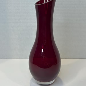 May include: A deep red glass vase with a rounded bottom and a narrow neck that flares out at the top.