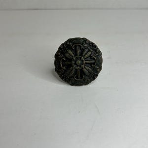 Op de afbeelding: Een ronde, bronzen metalen knop met een decoratief, kruisvormig ontwerp.