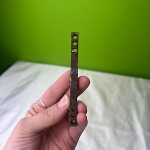 May include: A rusty metal bar with five evenly spaced circular holes. The bar is about 5 inches long and 1/2 inch wide.