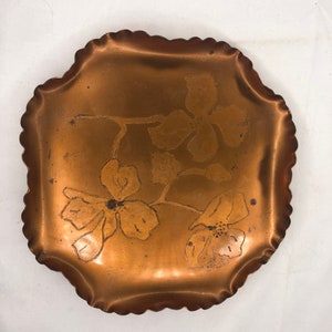 May include: A copper tray with a scalloped edge and a floral design. The tray is a light copper colour and the flowers are etched into the surface.