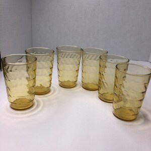 May include: Set of six amber glass tumblers with a textured design. The glasses are clear and have a slightly yellow tint.