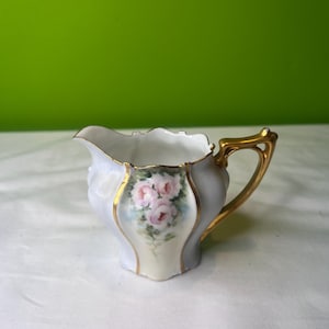 Jarra de porcelana vintage con diseño floral, detalles dorados y borde festoneado en la base, teñida en azul.