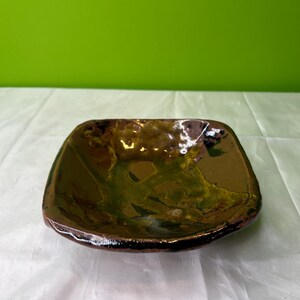 May include: A small, square ceramic dish with a brown, green, and white glaze. The dish has a slightly irregular shape and a textured surface.