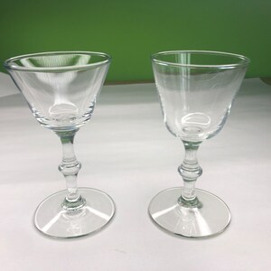 May include: Two clear glass stemmed drinking glasses with a wide bowl and a short, thick stem.