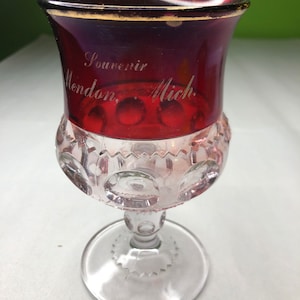 May include: A clear glass goblet with a red, gold-rimmed top. The goblet has a textured, bubble-like pattern and is inscribed with "Souvenir Mendon, Mich."