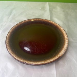 Peut inclure: Une assiette en céramique avec un centre marron foncé, passant à un bord marron plus clair. L'assiette a une finition brillante et convient pour servir des aliments. L'assiette est de forme ronde.