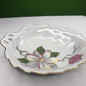 May include: White porcelain serving dish with a gold rim and a floral design. The dish is shaped like a leaf and has two cut-out handles.