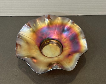 May include: An iridescent glass bowl with a ruffled edge. The bowl has a circular base and a flared, wavy rim. The colors shift from gold to purple and blue, creating a shimmering effect. The bowl is likely vintage or antique.