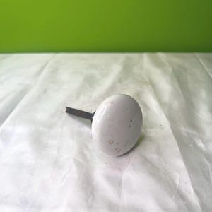 May include: White ceramic knob with brown speckles, attached to a black metal stem.