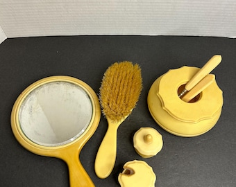 Può includere: Un set da toeletta vintage in plastica color avorio. Il set comprende uno specchio da mano, una spazzola per capelli, un piccolo contenitore rotondo con coperchio e due piccoli barattoli con coperchi.