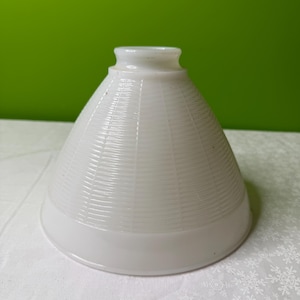 May include: A white, cone-shaped lampshade with a textured, ribbed design. The lampshade has a rounded base and a smaller, cylindrical top. The background is a solid green color.