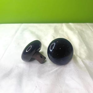 Könnte beinhalten: Zwei schwarze Keramik-Flaschenverschlüsse mit einer glatten, abgerundeten Oberseite und einer kleinen, flachen Basis.