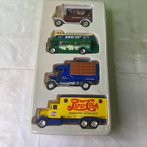 May include: A set of four vintage toy trucks in a plastic display case. The trucks are a red and white Good Humor ice cream truck, a green and yellow Zoo Tourist bus, a blue and white U.S. Mail truck, and a yellow and blue Pepsi-Cola truck.