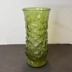 May include: A green glass vase with a textured, bubble-like design. The vase is tall and slender, with a rounded base.