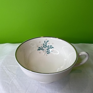 May include: White ceramic teacup with a green and pink floral design and a gold rim.