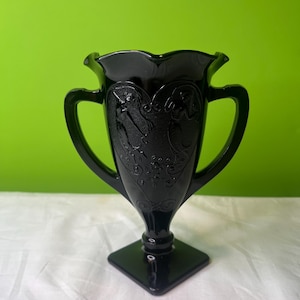May include: Black glass vase with two handles and a square base. The vase has an etched design of two figures and a heart.