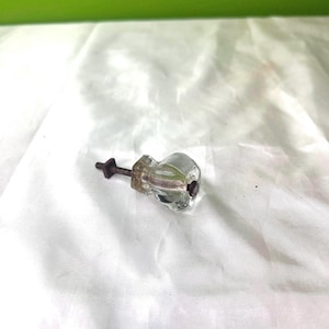 May include: A clear glass cabinet knob with a metal screw. The knob has a faceted design and a slightly rounded shape.