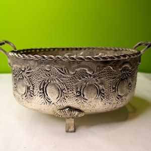 Peut inclure: Bol en argent de forme ovale avec des motifs floraux et de vigne détaillés. Le bol a deux petites poignées et repose sur un seul pied. Le bord présente un motif de corde torsadée.