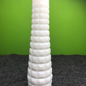 May include: A tall, white, vintage vase with a textured, ridged design. The vase is cylindrical with a slightly flared top and a rounded base. The white color gives it a clean, classic look. The vase is approximately 10 inches tall.