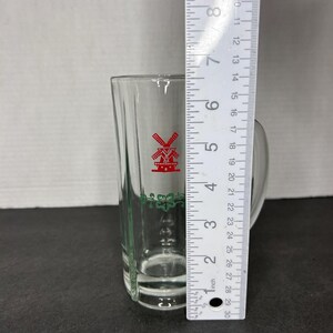 May include: A clear glass shot glass with a green and red windmill design. The glass is approximately 5 inches tall.