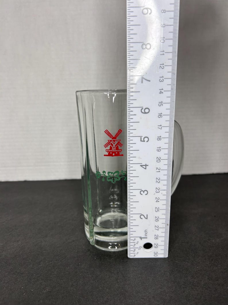 May include: A clear glass shot glass with a green and red windmill design. The glass is approximately 5 inches tall.