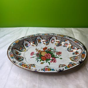 Puede incluir: Bandeja ovalada de metal para servir con diseño floral. La bandeja presenta un fondo blanco con un ramo central de flores rosas, naranjas y amarillas. El borde tiene un patrón de enrejado con acentos florales coloridos y un borde dorado.