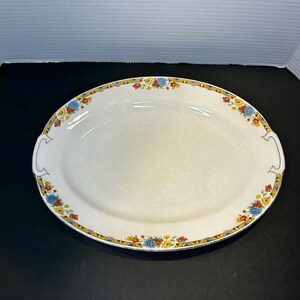 May include: A white oval serving platter with a floral design in shades of blue, yellow, and orange. The platter has a gold trim and two handles.