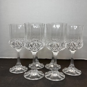 May include: Set of six clear glass wine glasses with a cut crystal design. The glasses have a tall, slender stem and a round base.