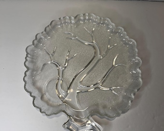 Puede incluir: Un plato de servir de vidrio transparente con forma de árbol y superficie texturizada. El plato tiene una base elevada y un diseño de árbol con ramas.