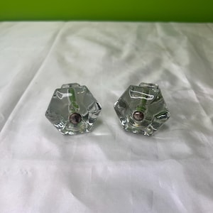 Puede incluir: Dos pomos de armario de vidrio transparente con forma hexagonal y un tornillo de metal plateado en el centro.