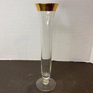 May include: A clear glass vase with a gold rim and a flared base. The vase is tall and slender.