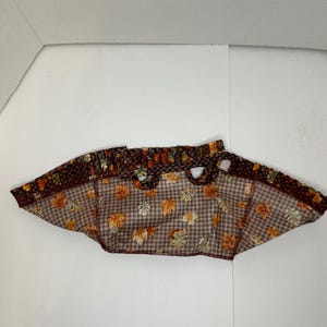 May include: A brown and tan fabric tote bag with a checkered pattern and a leaf print. The bag has two handles and a wide opening.