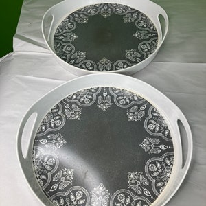 Puede incluir: Dos bandejas redondas blancas para servir con diseños de patrones en blanco y negro. Las bandejas tienen asas blancas.