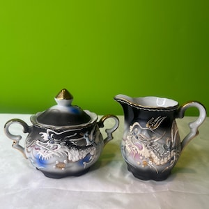 May include: A black and white porcelain creamer and sugar bowl set with gold accents. Both pieces feature a detailed dragon design.
