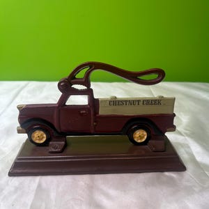 Peut inclure: Un casse-noix en fonte de couleur marron en forme de camionnette vintage. La benne du camion est beige avec l'inscription "CHESTNUT CREEK". Les roues sont dorées et le levier du casse-noix est marron.