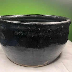 May include: A large, black ceramic bowl with a slightly uneven rim. The bowl has a glossy finish and is slightly wider at the top than the bottom.