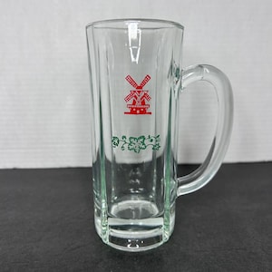 May include: A clear glass beer mug with a handle. The mug has a red windmill design with green vines around the bottom.