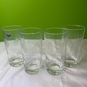 Op de afbeelding: Vier heldere, geëtste highballglazen met bloemmotieven. De glazen zijn cilindrisch met een licht uitlopende rand. De ets bevat een delicaat patroon van bladeren en bloemen. De glazen worden gepresenteerd op een wit oppervlak tegen een groene achtergrond.